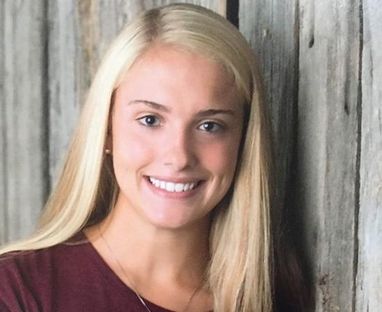 Isabelle LaBelle '23, stands in front of a wooden door, smiling.